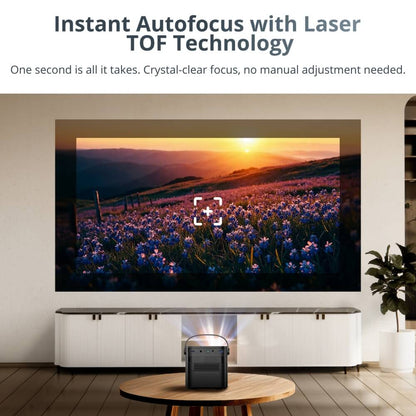Digital advertisement of a black portable projector on a round wooden coffee table in a modern living room projecting a vibrant sunset over a field of purple flowers and rolling hills onto a wall, featuring a white autofocus target icon demonstrating laser TOF technology