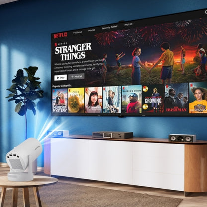 Photograph of a white projector casting a blue light beam onto a blue wall where a large smart TV displays Netflix's Stranger Things with colorful fireworks, positioned above a modern white and wood media console in a contemporary living room