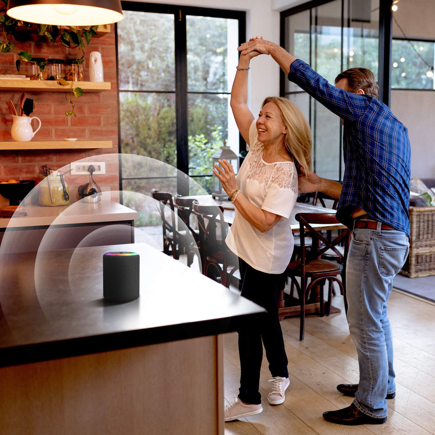 Dancing couple in a modern kitchen with a smart speaker featuring a colorful light ring on the counter, a brick wall backsplash, and large windows