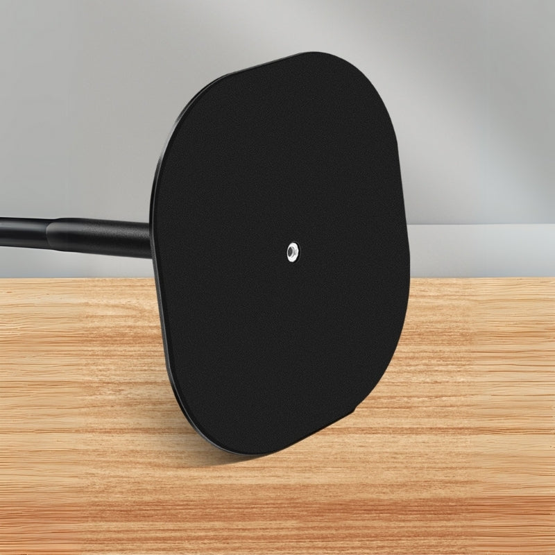 Photograph of a matte black roughly oval stand base featuring a central silver screw attached to a black rod, resting on a light wood surface against a simple grey wall