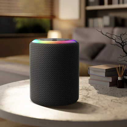 A smart speaker with a vibrant rainbow LED ring and black fabric grille on a coffee table in a modern living room beside a stack of books and a reed diffuser