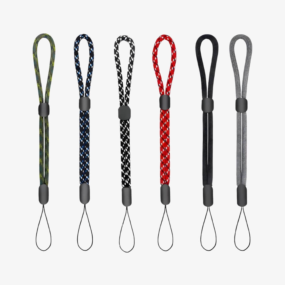 Photography of six braided wrist straps featuring adjustable black sliders and diverse patterns including green camouflage, blue geometric, red geometric, solid black, and solid grey