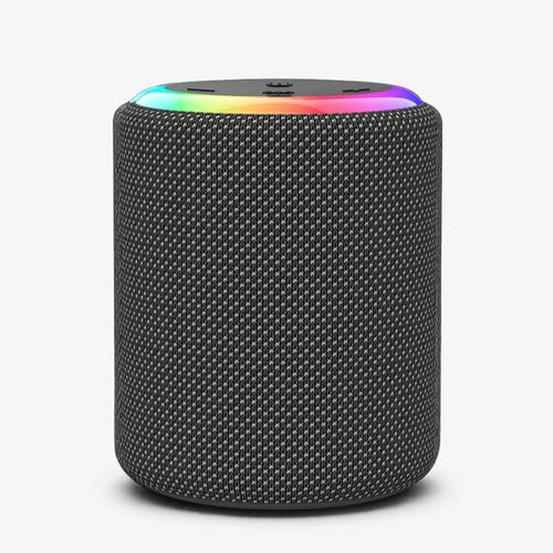 Photograph of a cylindrical portable Bluetooth speaker with a dark grey fabric mesh exterior isolated on a white background featuring a vibrant rainbow LED light ring around its top edge and subtle control buttons