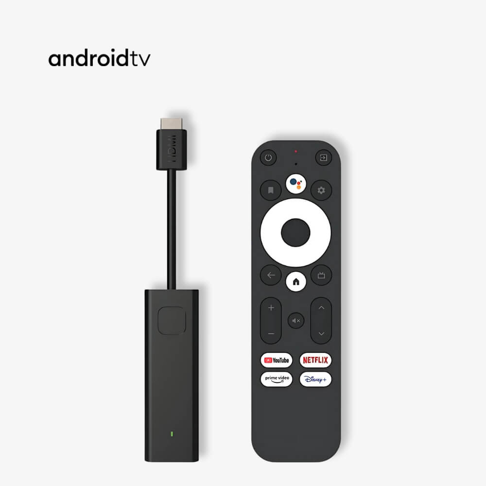 Product image of an Android TV streaming dongle and remote control on a plain white background, featuring a black HDMI stick, a dark grey remote with a white circular directional pad, and colorful app buttons for YouTube Netflix Prime Video and Disney+